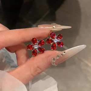 Close-up detail of elegant red flower zircon stud earrings held between manicured fingers