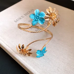 Nahaufnahme eines goldenen Blumen-Armreifs mit leuchtend blauen Emaille-Blüten