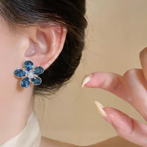 Detailed view of elegant blue crystal flower stud earrings worn on a model's ear