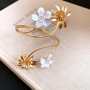 Detailansicht eines eleganten goldenen Blumen-Armreifs mit weißem Emaille-Design.