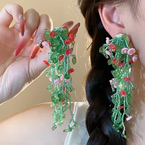 Detailed close-up of handmade green glass leaf and flower tassel earrings on model.