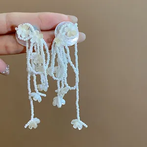 Close-up detail of elegant white glass flower earrings featuring long beaded tassels