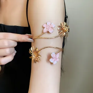 Nahaufnahme eines goldenen Oberarmreifs mit rosa Emaille-Blumen an einem Model