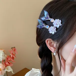 Dettaglio di fermagli in resina con coda di sirena e fiori su capelli intrecciati