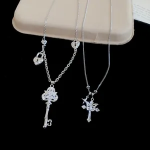 Gros plan de colliers en argent avec pendentifs clé et croix en zircone sur noir.
