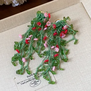 Close-up of forest-style green glass leaf earrings with pink flowers on silver needles.