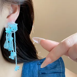 Close-up view of a blue glass flower tassel earring worn on ear with summer vibes