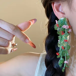 Close-up detail of forest style tassel earrings with green glass leaves and pink flowers