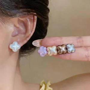 Close-up of shell-like flower stud earrings in multiple colors on a model's ear.