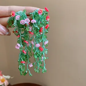 Detailed view of beaded green leaf and pink floral tassel earrings with silver needles