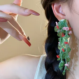 Detailed macro view of forest style glass leaf and flower tassel earrings worn by model