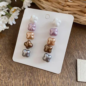 Close-up of five pairs of pearlescent flower stud earrings in varied colors on a white display card