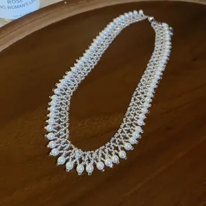 Detailed view of handmade pearl fringe necklace with intricate beadwork on wooden tray