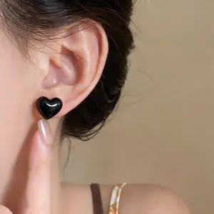 Close-up macro shot of elegant glossy black heart-shaped stud earring worn on an earlobe