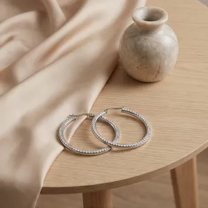 Détail de grandes boucles d'oreilles créoles en acier avec pavage de zircons brillants.