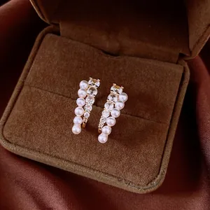 Primer plano de pendientes dorados con filas de perlas blancas y circonitas brillantes.