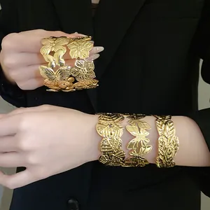 Detailed view of gold butterfly and floral cuff bracelets worn on black blazer background