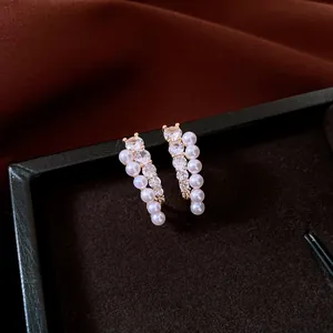 Vista detallada de elegantes pendientes de botón con pequeñas perlas y circonitas brillantes.