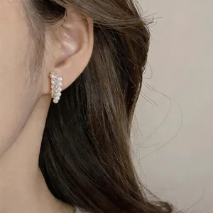 Primer plano de pendientes de botón con circonitas y perlas puestos en la oreja