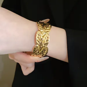 Detailed close-up of a gold ruffled leaf open bangle worn on a model's wrist.