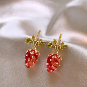 Detailed close-up view of red strawberry stud earrings with gold leaves and pearl accents