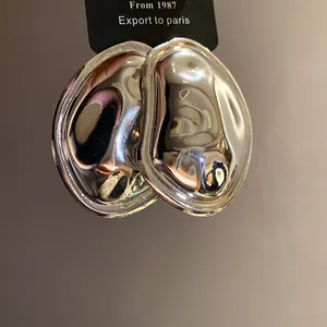 Close-up view of silver metallic oval earrings featuring a unique textured pleated design