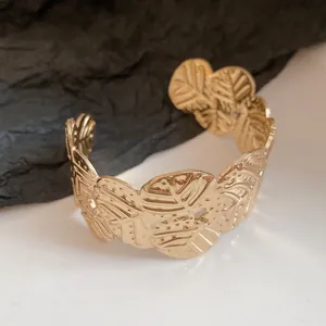Detailed view of a gold-plated metal cuff bracelet with leaf-like textures and patterns.