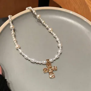 Close-up detail of a white pearl beaded necklace with a hammered gold cross pendant