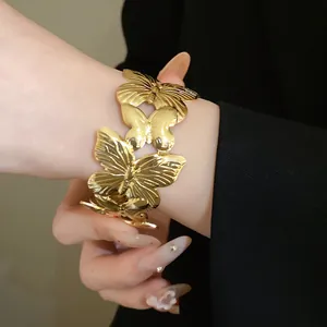 Detailed view of an elegant gold pleated metal butterfly open cuff bracelet on a wrist.