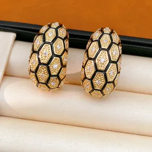 Détail de boucles d'oreilles en C dorées 18 carats avec motif nid d'abeille noir
