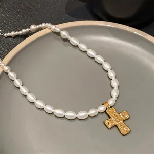 Close-up detail of an elegant oval pearl necklace featuring a textured gold cross pendant.