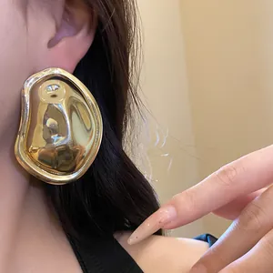 Detailed view of oversized golden metallic oval earrings with lava texture worn by a model