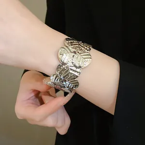 Close-up detail of a silver metallic cuff bracelet featuring textured butterfly joint designs