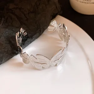 Detailed view of silver metal pleated butterfly open cuff bracelet on white plate