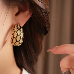 Gros plan d'une boucle d'oreille en forme de C avec motif nid d'abeille et zircons