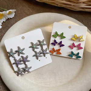 Primer plano de pendientes esmaltados de estrella de mar y mariposa en colores vivos.
