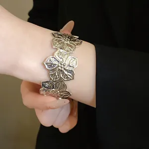 Detailed shot of a silver floral textured metal open cuff bracelet on female wrist.