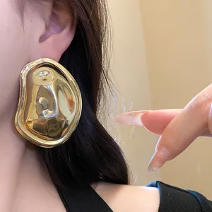 Close-up of gold crumpled metal oval earring on ear showing glossy metallic texture