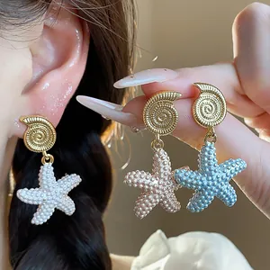 Detalle de pendientes de estrella de mar y concha bañados en oro de 18k estilo playa