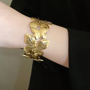 Detailed macro view of a gold-toned metal open bracelet with pleated butterfly charms