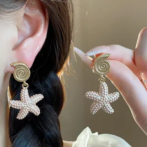 Vista macro detallada de pendientes colgantes de concha y estrella de mar dorados