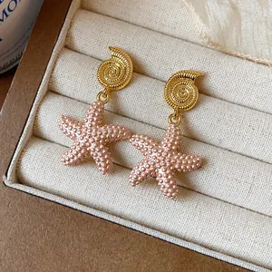 Primer plano detallado de pendientes de estrella de mar y concha bañados en oro