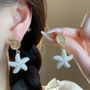 Detalle de pendientes colgantes de concha y estrella de mar chapados en oro de 18 quilates