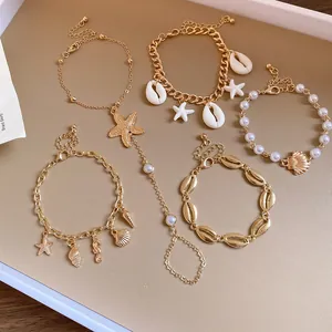 Detailed close-up of bohemian gold-tone bracelets featuring shell, starfish and pearl charms.