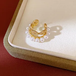 Primer plano de un elegante ear cuff dorado de doble capa con perlas y circonitas.