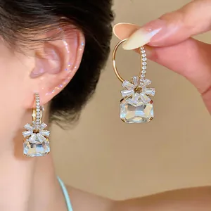 Detailansicht funkelnder geometrischer Zirkonia-Creolen in Blumenform am Ohr und in der Hand