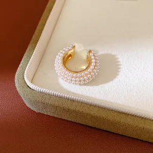 Detalle macro de un elegante ear cuff dorado en forma de C con microperlas dobles