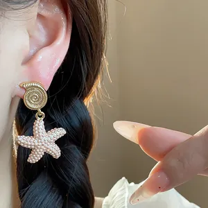 Primer plano de elegantes pendientes de concha y estrella de mar chapados en oro 18k