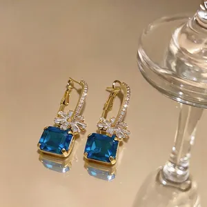 Makroaufnahme von Blumenohrringen mit blauen Edelsteinen im Smaragdschliff und Goldfinish.