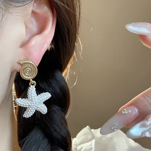Detalle macro de pendientes colgantes de concha y estrella de mar dorada